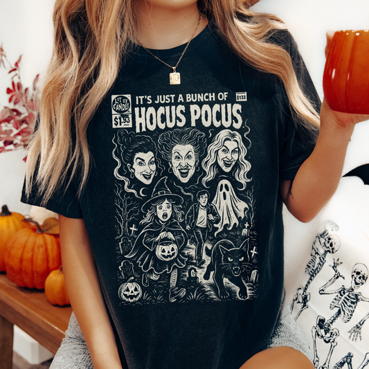 Person wearing a black t-shirt with Hocus Pocus design, holding a pumpkin in a festive setting.