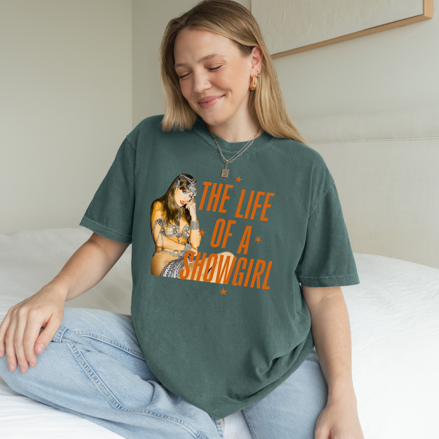Woman wearing a green t-shirt with a graphic and text, sitting on a bed.