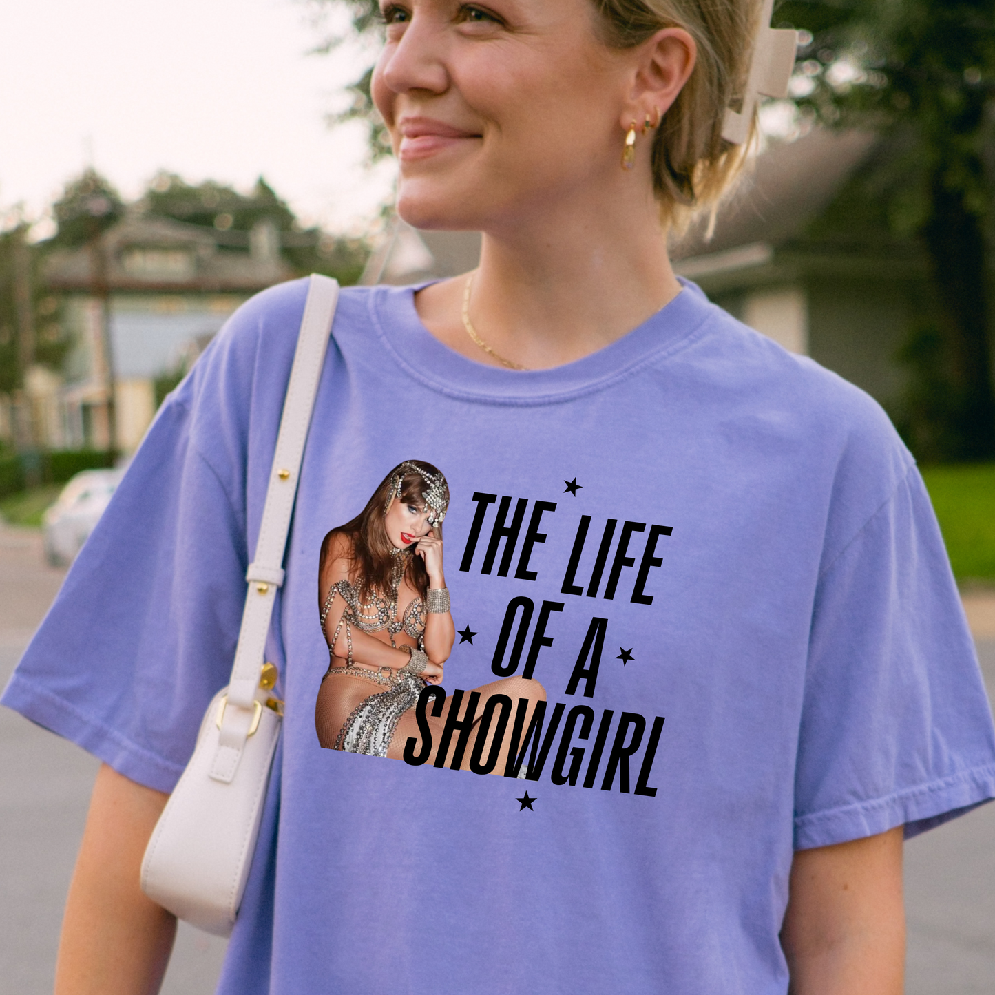 Woman wearing a purple t-shirt with a graphic and text 'Showgirl' outdoors.