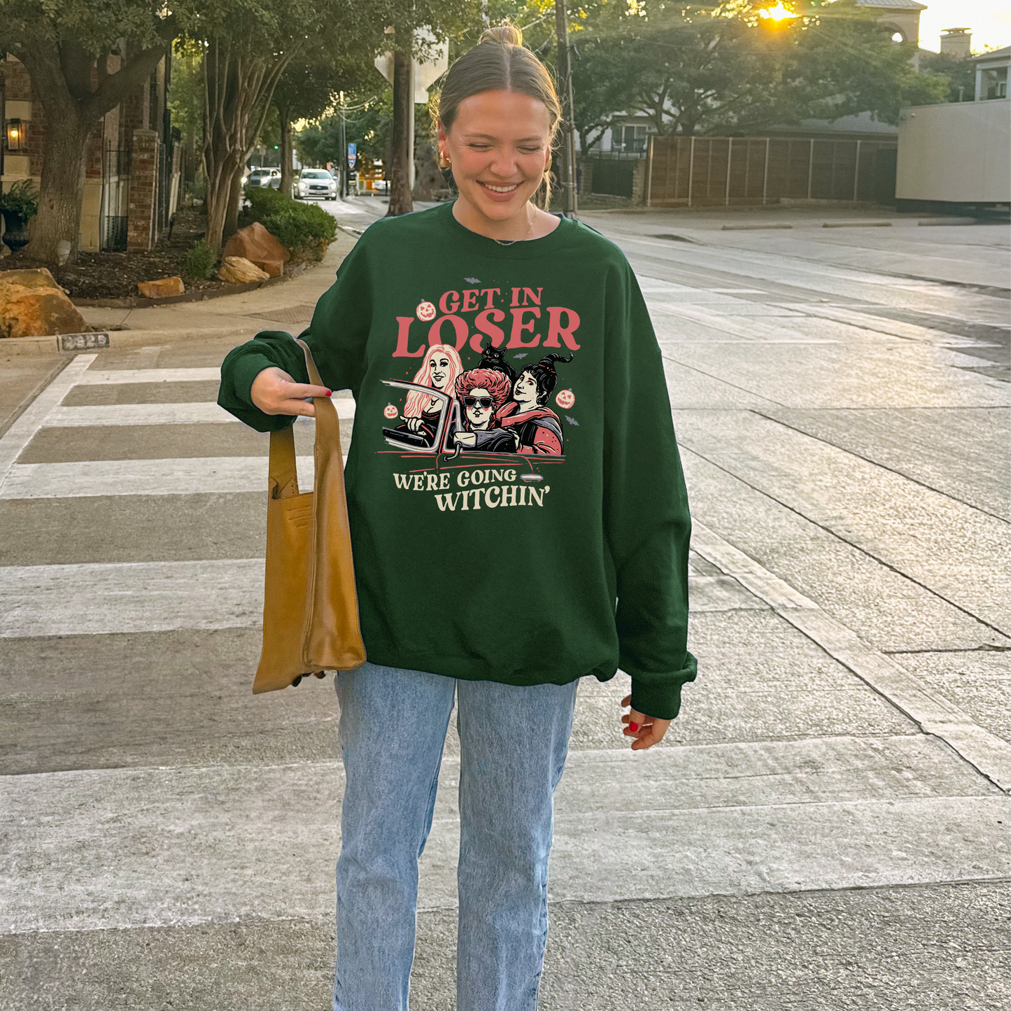 Person wearing a green sweatshirt with halloween graphic design and text, standing on a sidewalk.