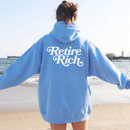 Person wearing a blue hoodie with 'Retire Rich' text on the beach