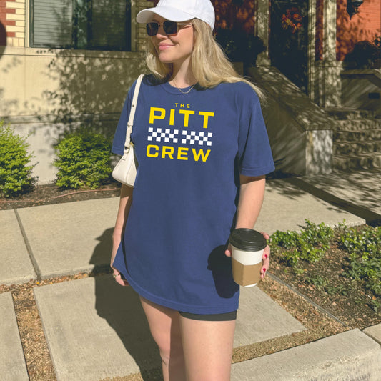 Woman wearing a blue 'PITT CREW' t-shirt holding a coffee cup outdoors.