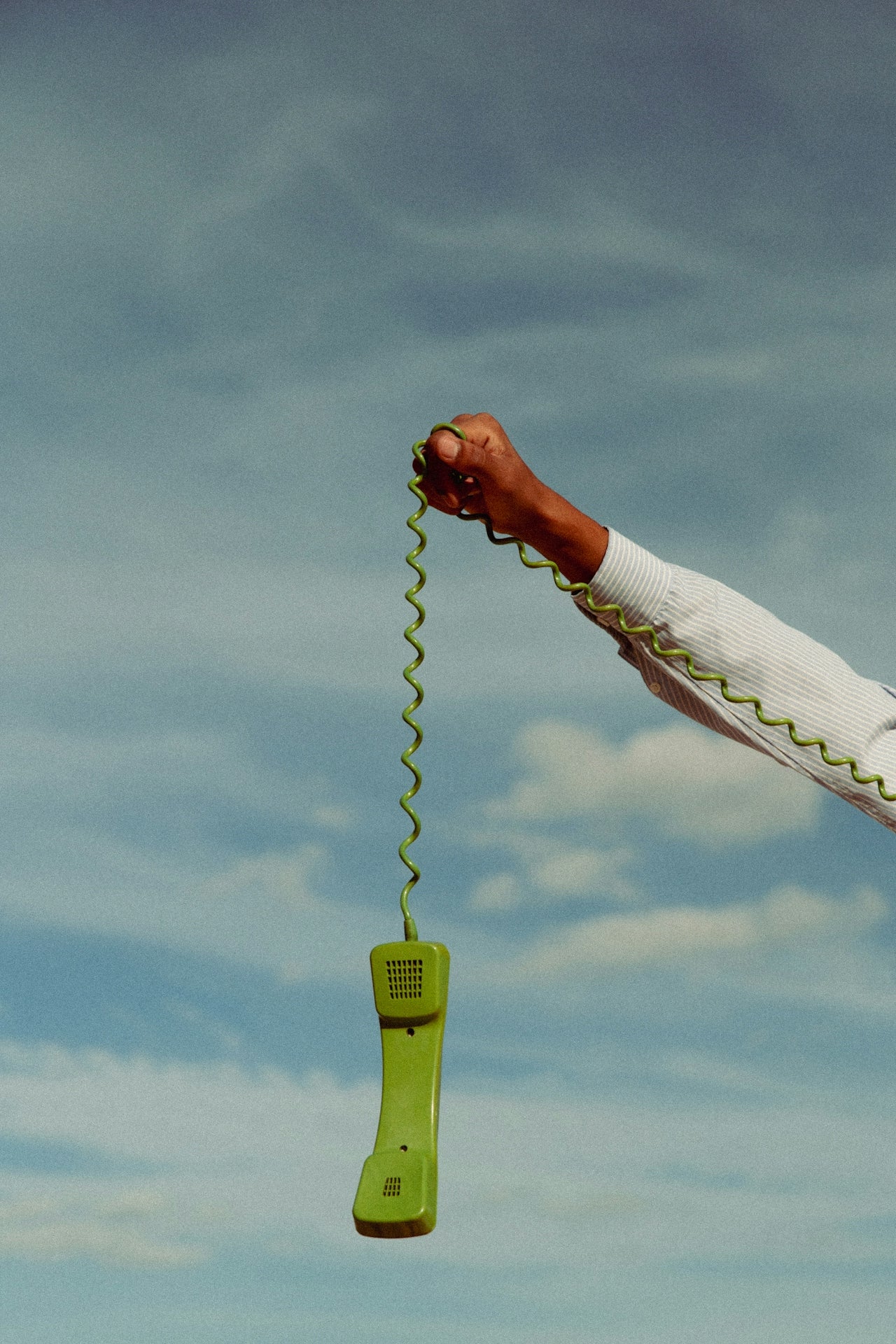 Green phone receiver held against a blue sky with clouds
