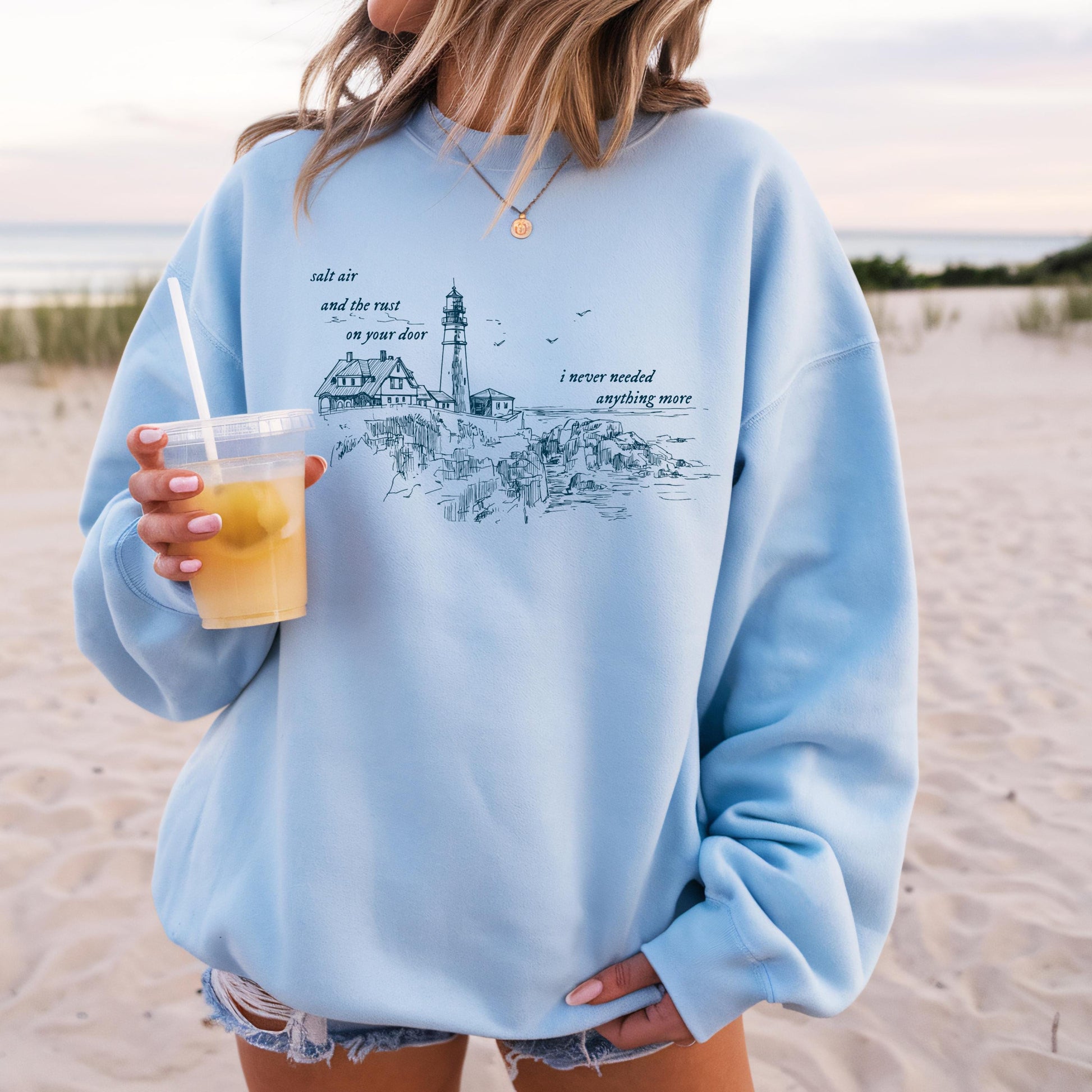 Person wearing a light blue sweatshirt with a beach scene design on a sandy background