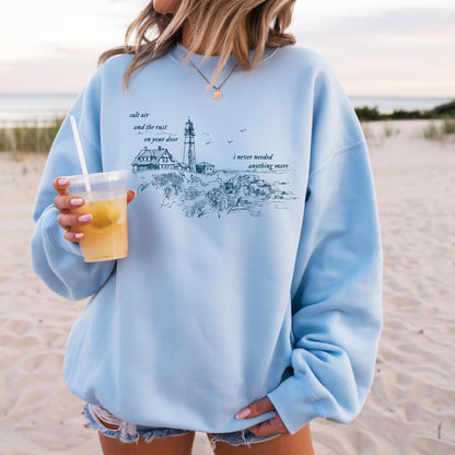 Person wearing a light blue sweatshirt with a beach scene design on a sandy background
