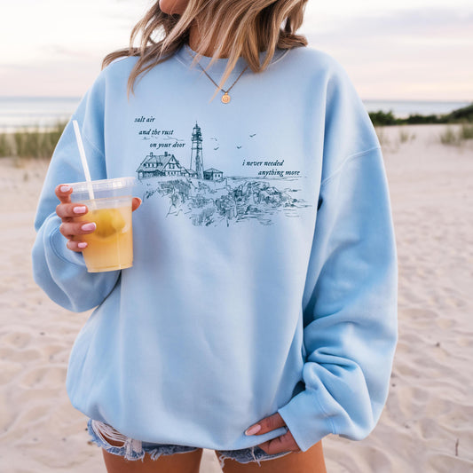 Person wearing a light blue sweatshirt with a beach scene design on a sandy background