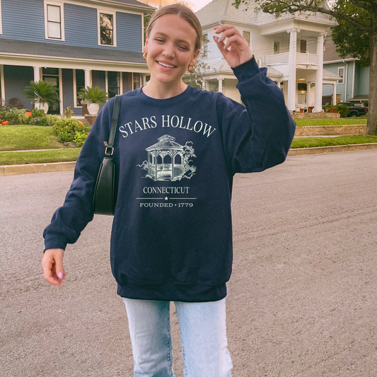 Person wearing a navy blue sweatshirt with 'Stars Hollow Connecticut' print, standing on a street.